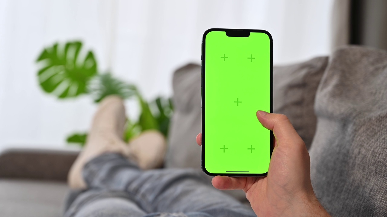 躺在沙发上刷绿屏智能手机的男子。社交媒体、快递、健康、在线购物应用等视频素材