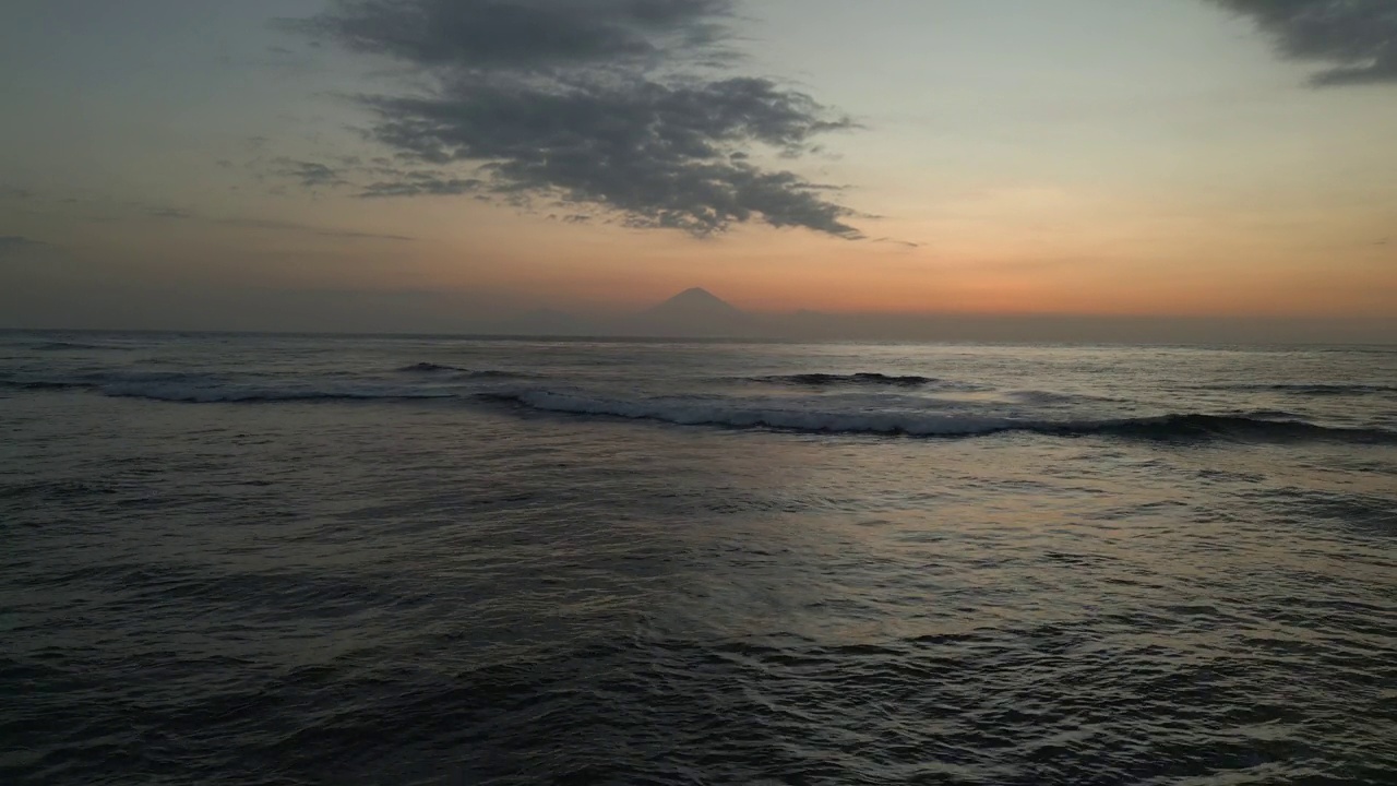 落日拍打着海浪，地平线上有山的剪影视频素材