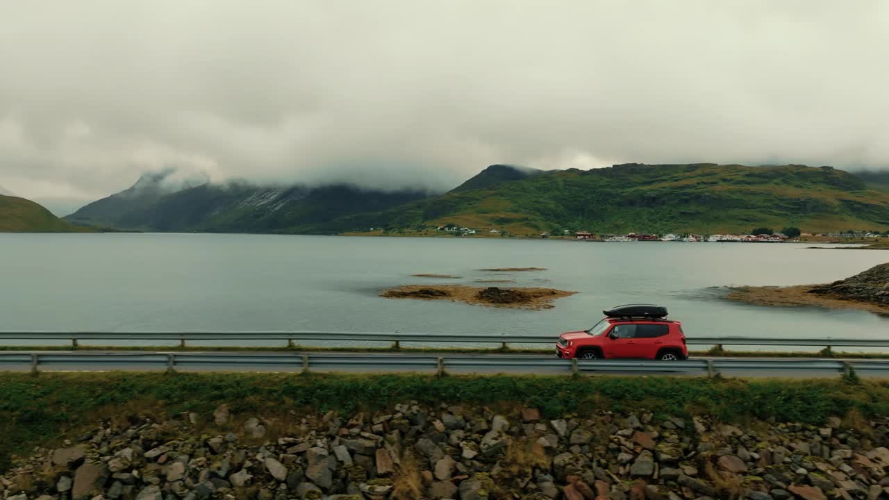 无人机跟随一辆红色SUV沿着海岸公路行驶，背景是风景如画的斯堪的纳维亚风景视频素材