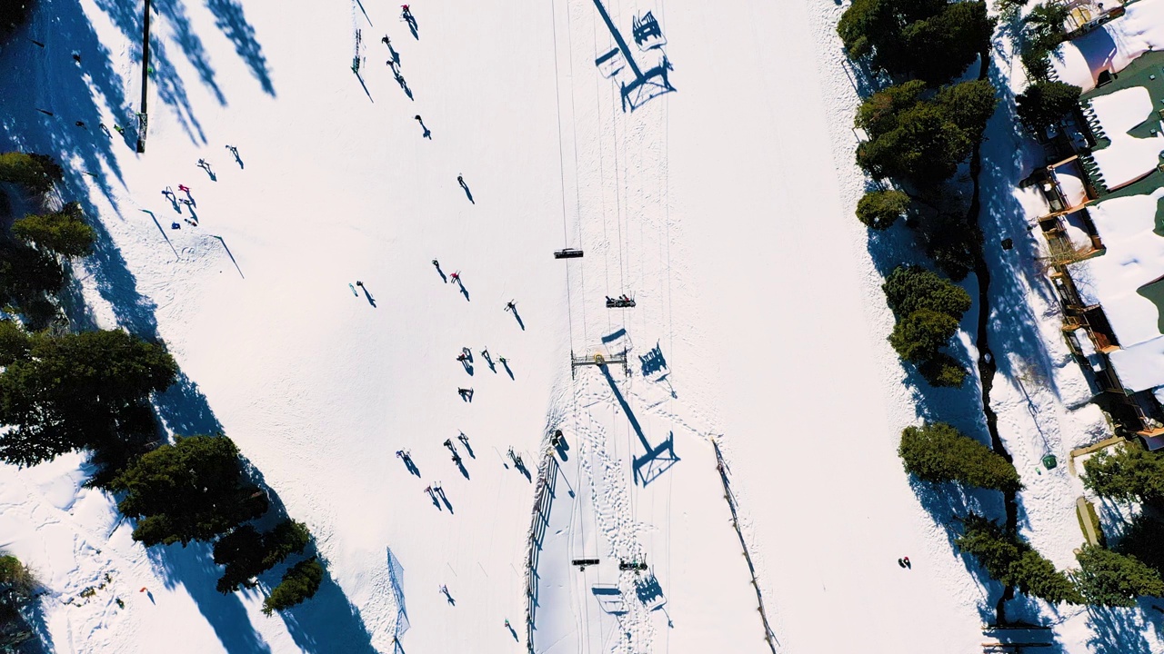 在厚厚的粉雪中滑雪和乘坐缆车的人们的上图。无人机航拍画面视频素材