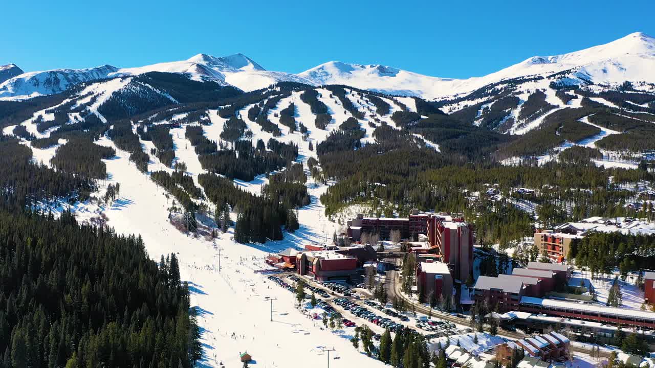 空中无人机观看巨大的滑雪胜地，人们在完整的停车场滑雪，乘坐缆车从山坡上滑下，穿过白雪覆盖的松树林视频素材