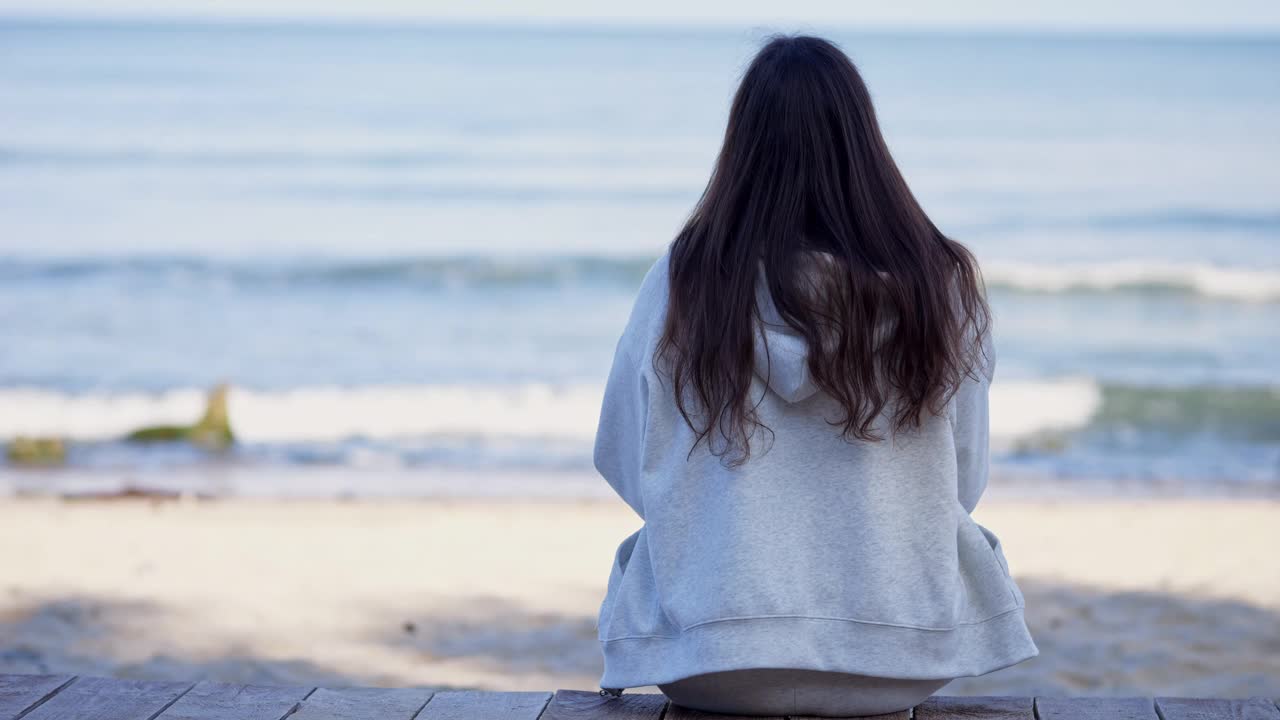 女人坐在长凳上，看着清澈的海浪视频下载