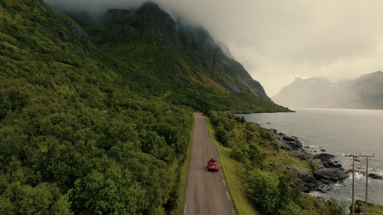 红色SUV行驶在美丽的绿色斯堪的纳维亚风景的沿海道路上视频素材