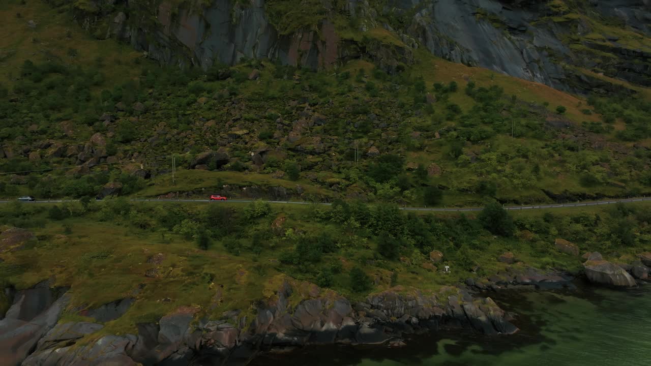 鸟瞰图红色SUV行驶在美丽的海滨道路在绿色岩石峡湾景观视频素材