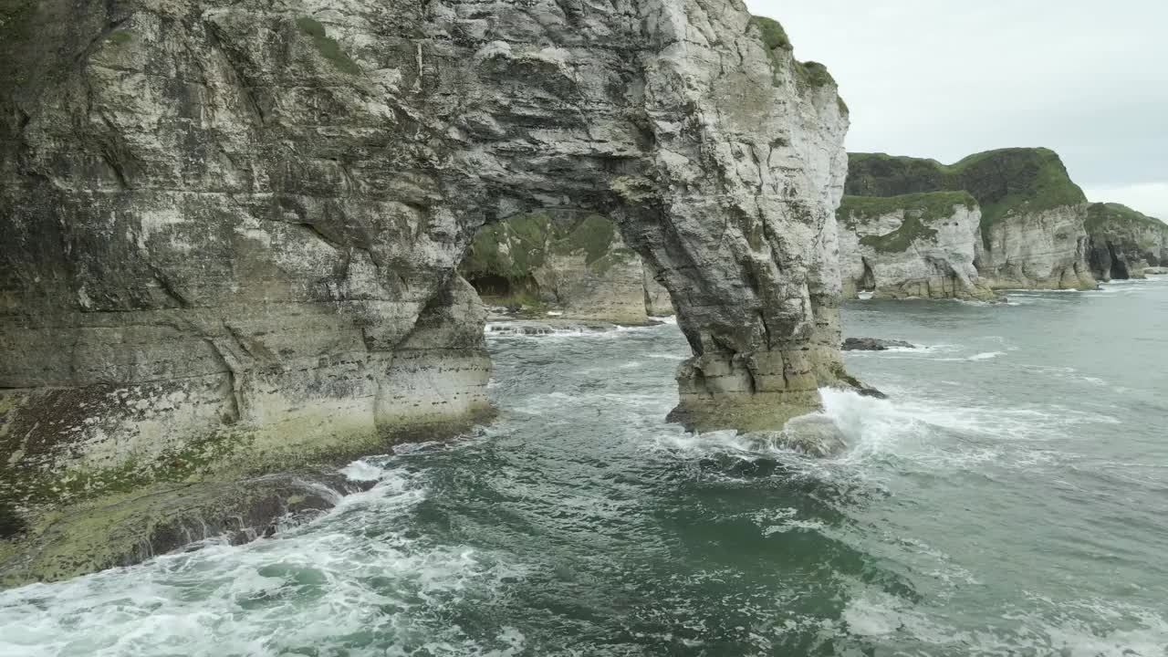 在北爱尔兰安特里姆郡的一个阴天，无人机飞过海岸白色悬崖拱门。low-aerial视频素材