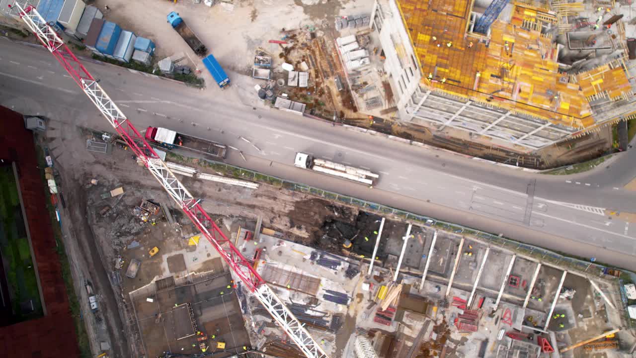 鸟瞰熙熙攘攘的建筑工地，高耸的起重机、机械和旁边的城市街道。视频素材