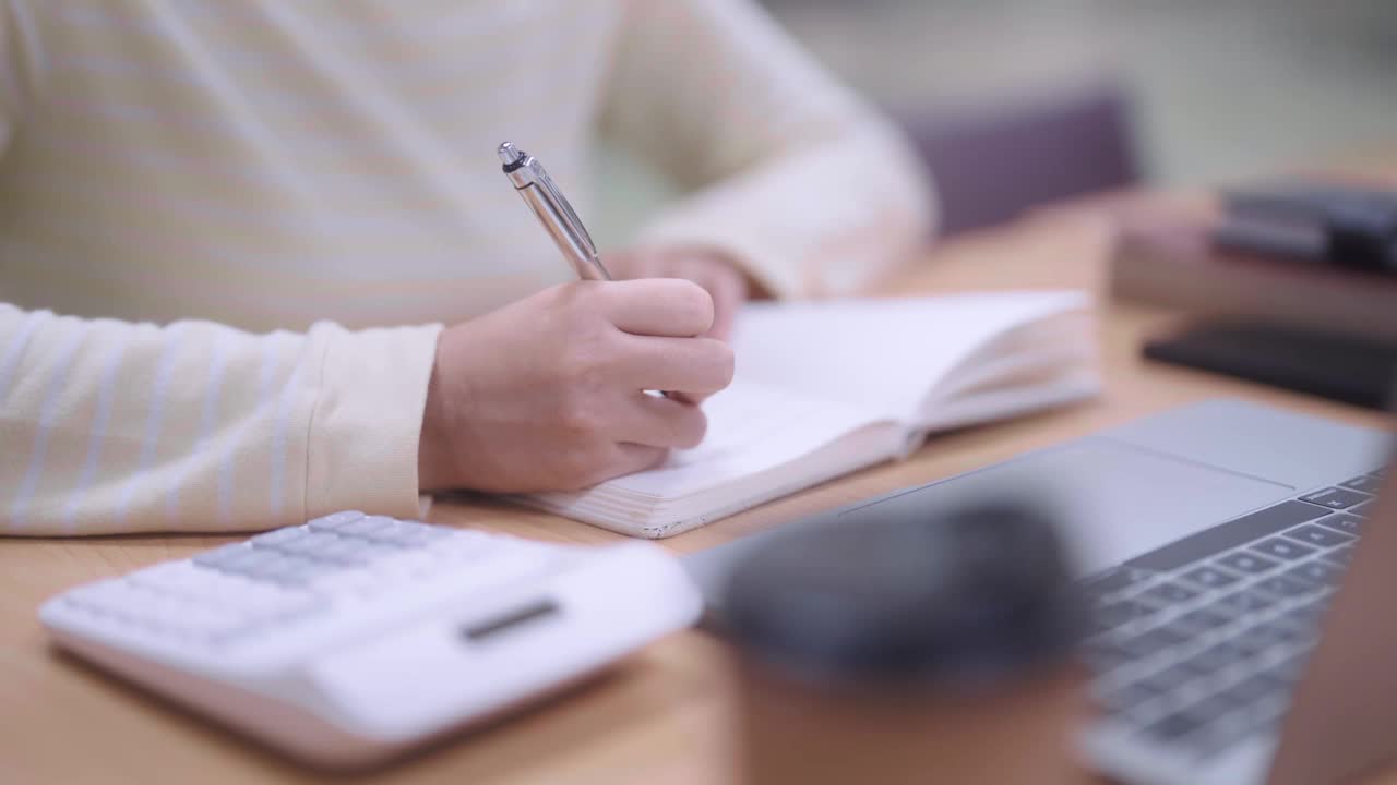 一个勤奋的亚洲女学生在学校或大学图书馆里忙着总结她所学的课程或准备考试。她专注于她的工作，利用安静的空间视频素材