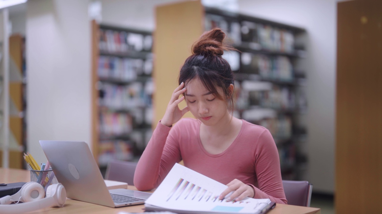 在学校或大学图书馆，一名紧张的亚洲女学生在试图理解困难的学习材料时显得困惑和焦虑。她感到不知所措视频素材