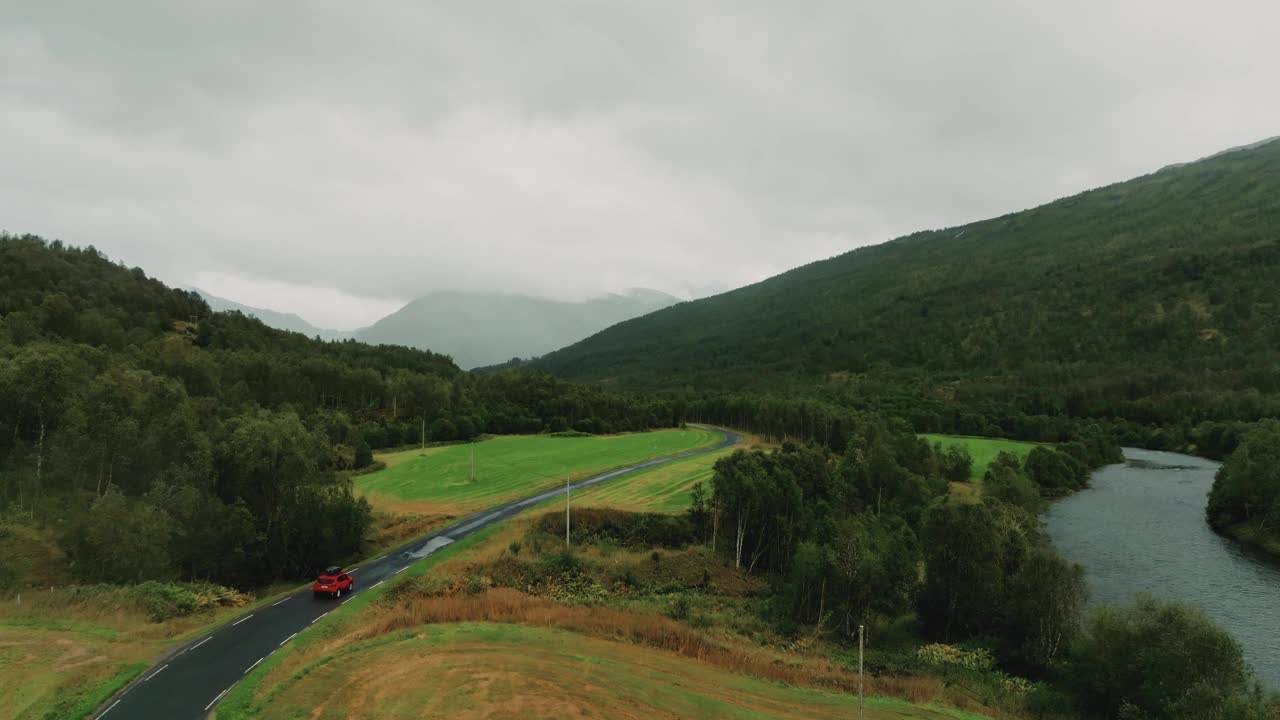 北欧大自然美丽的乡村全景配上红色轿车，驾车穿过森林视频素材