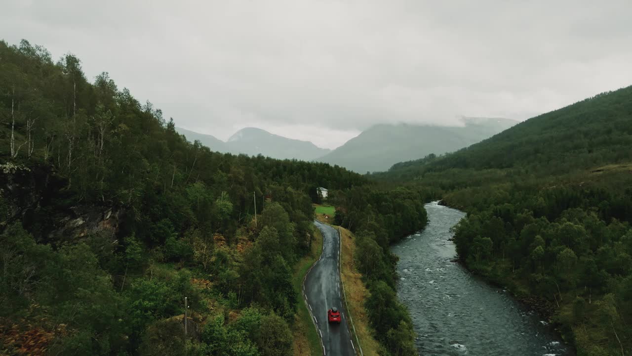 下雨天，一辆红色SUV轿车行驶在斯堪的纳维亚乡村的乡间小路上视频素材