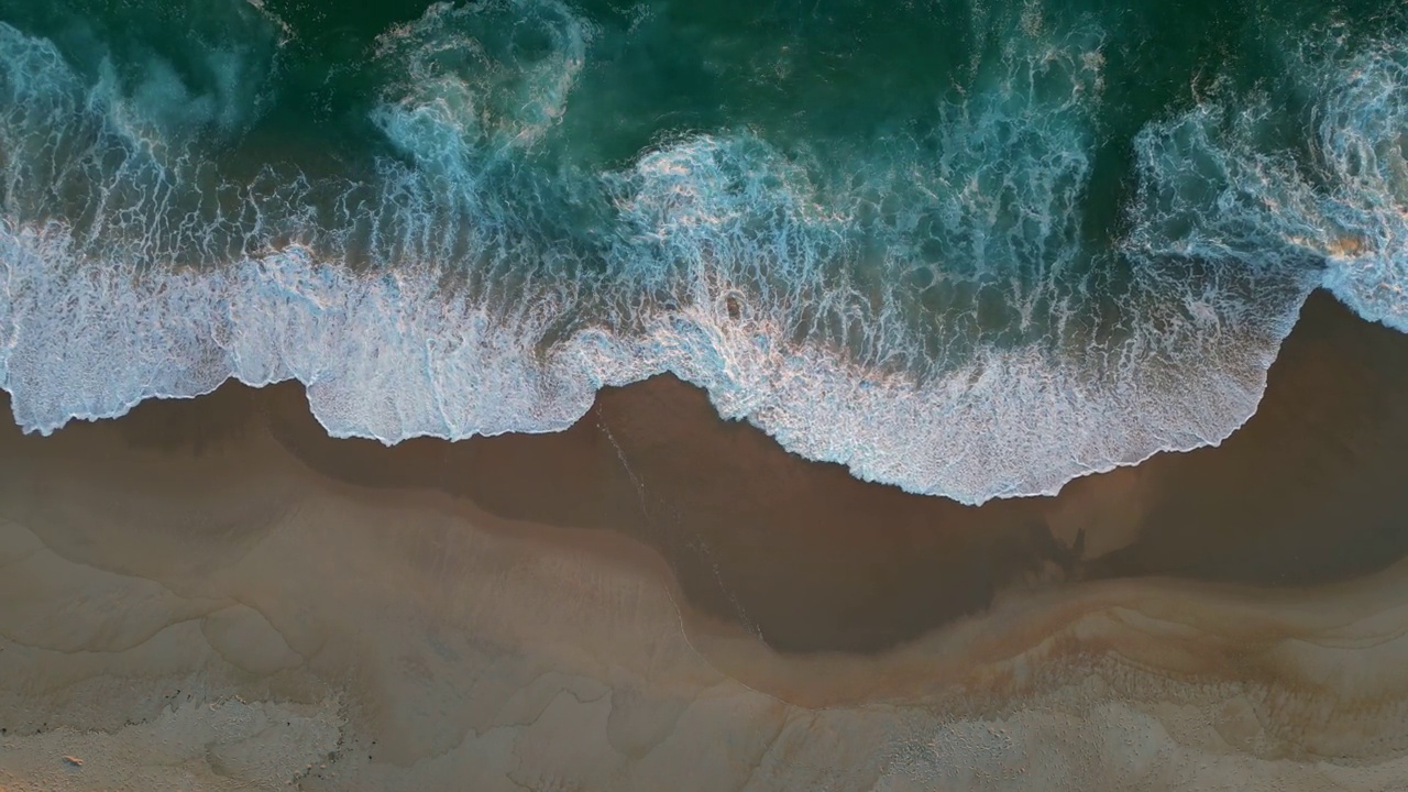 日落时分，沙滩上的浪花泛起白色泡沫。空中俯瞰海景或海洋沙滩视频素材