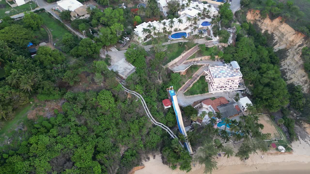 珊瑚海滩无人机视频，其郁郁葱葱的植被和自然，以及住宅和酒店栖息在周围的山脉在埃斯孔迪多港，墨西哥瓦哈卡州视频素材