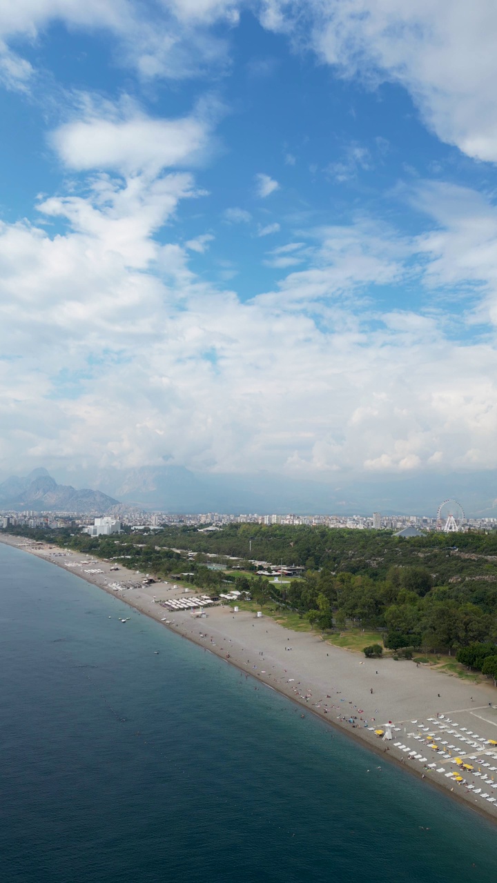 鸟瞰土耳其安塔利亚的konyaaltai海滩。一群人在海里游泳，在海滩上晒日光浴。雄伟的山脉与阴霾的背景。在土耳其度假视频素材