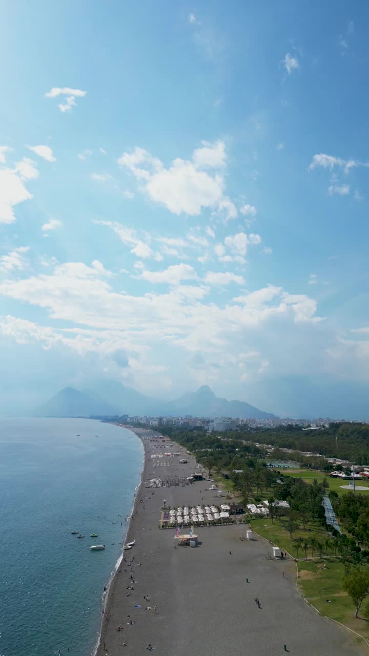 鸟瞰土耳其安塔利亚的konyaaltai海滩。一群人在海里游泳，在海滩上晒日光浴。雄伟的山脉与阴霾的背景。在土耳其度假视频素材