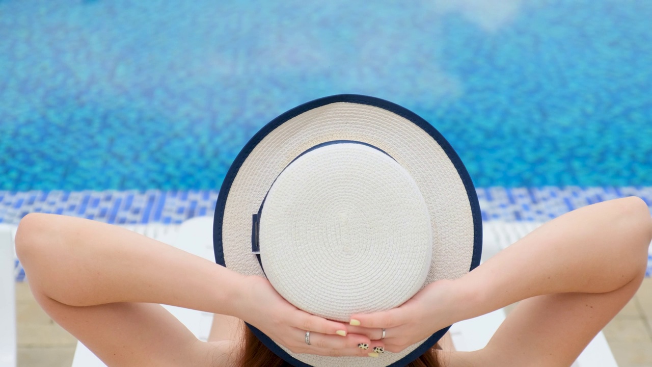 一个戴着帽子的女孩在夏季室外游泳池边休息。视频素材