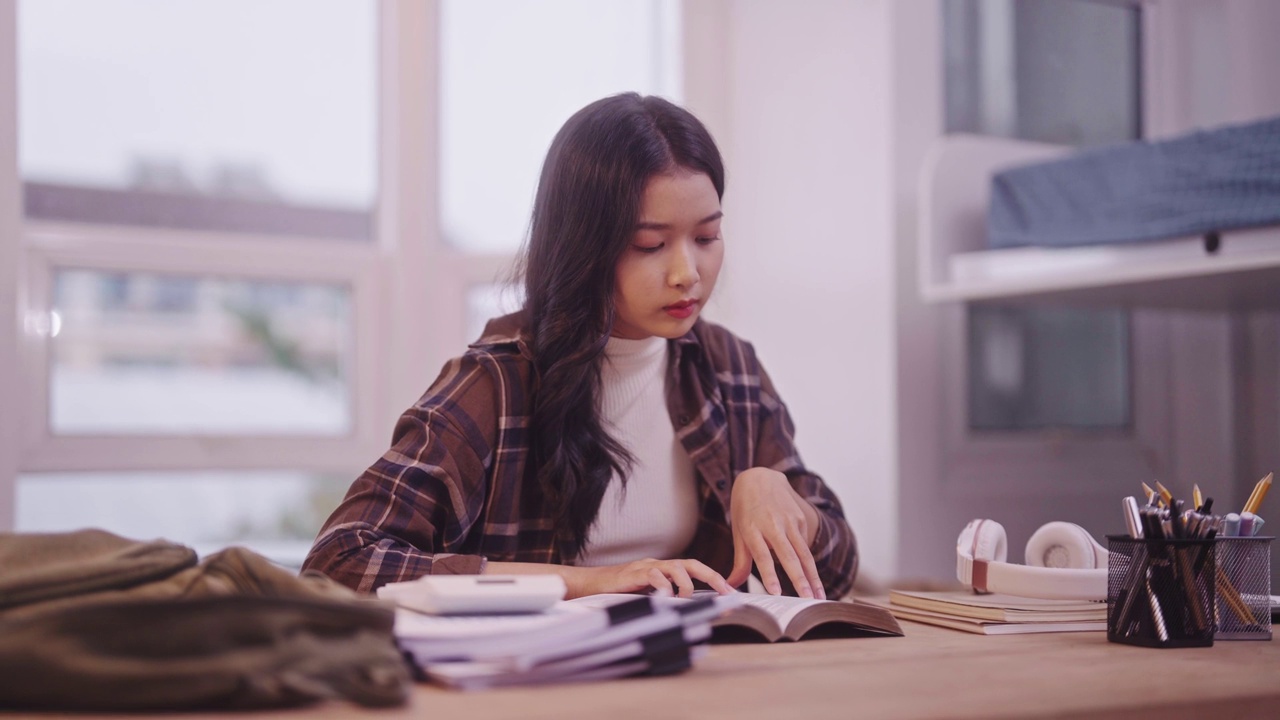 身着学习服的亚洲女学生正埋头读书，为即将到来的考试做着勤奋的准备。她的承诺是如此坚定，以至于她发现自己在宿舍的桌子上打瞌睡。视频素材