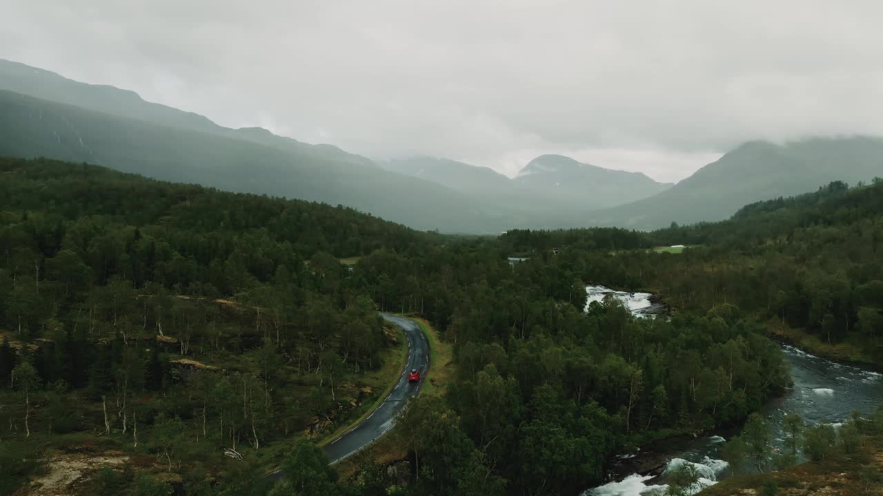 史诗航拍美丽的绿色北欧景观在雨天。红色SUV行驶在野河附近的路上视频素材