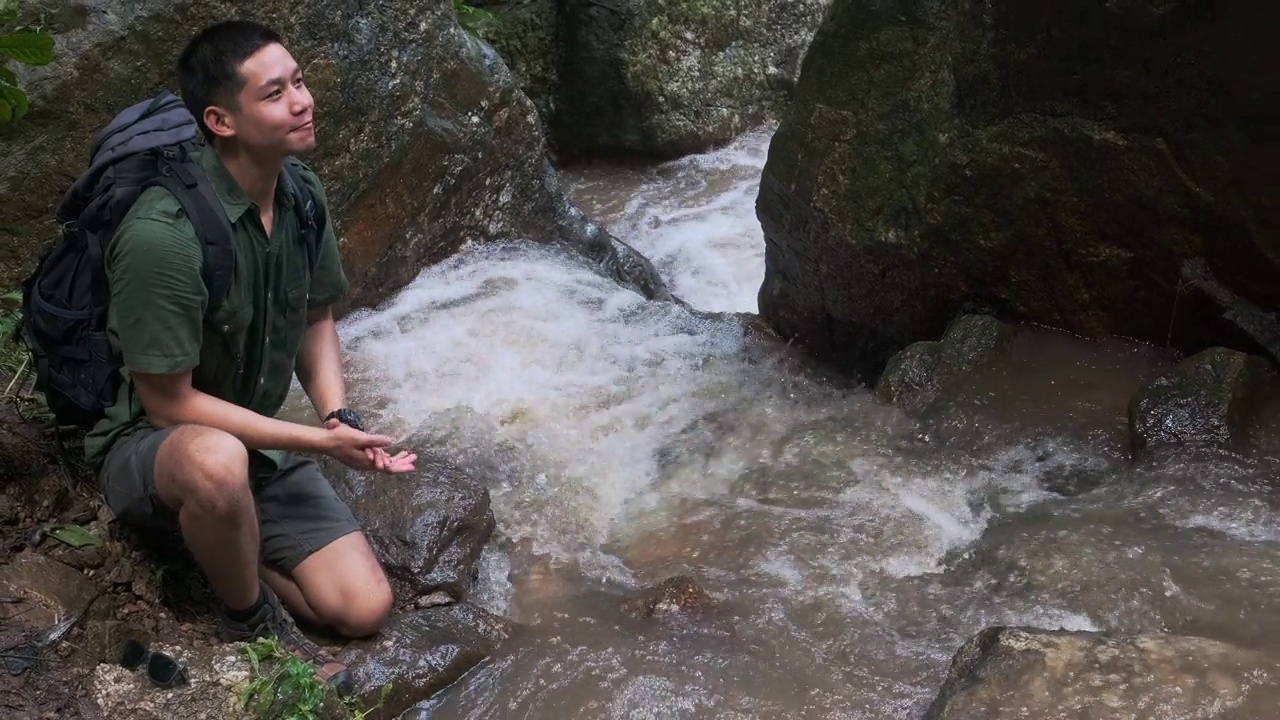 快乐的男徒步旅行者用山间小溪的水洗脸。视频素材