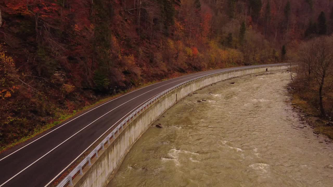 鸟瞰图，一辆汽车行驶在公路上，穿过山间河流，背景是秋天的森林视频下载