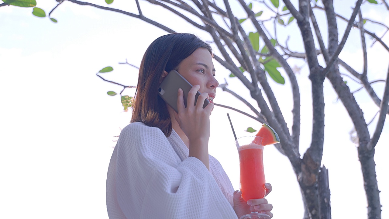 度假时，年轻女子拿着西瓜汁在泳池边打电话视频下载