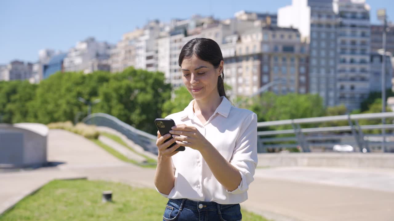 布宜诺斯艾利斯，一名拉丁女子一边看着镜头，一边举起拳头，手里拿着智能手机视频下载