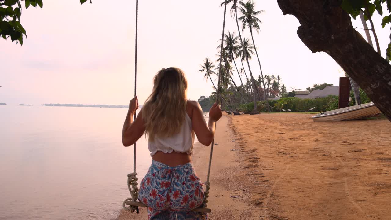 慢镜头:在热带海滩度假的女人在海滩上荡秋千视频素材