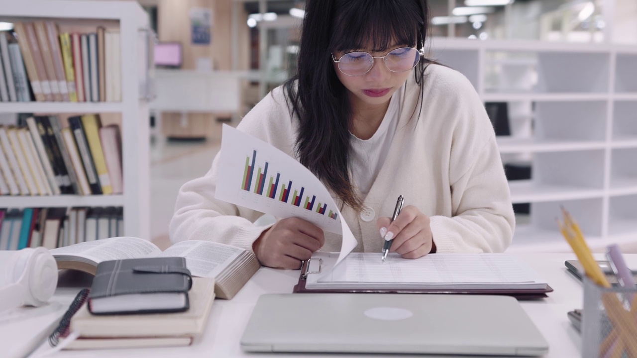 亚洲女大学生正在大学图书馆认真复习课程，准备作业或考试。视频素材