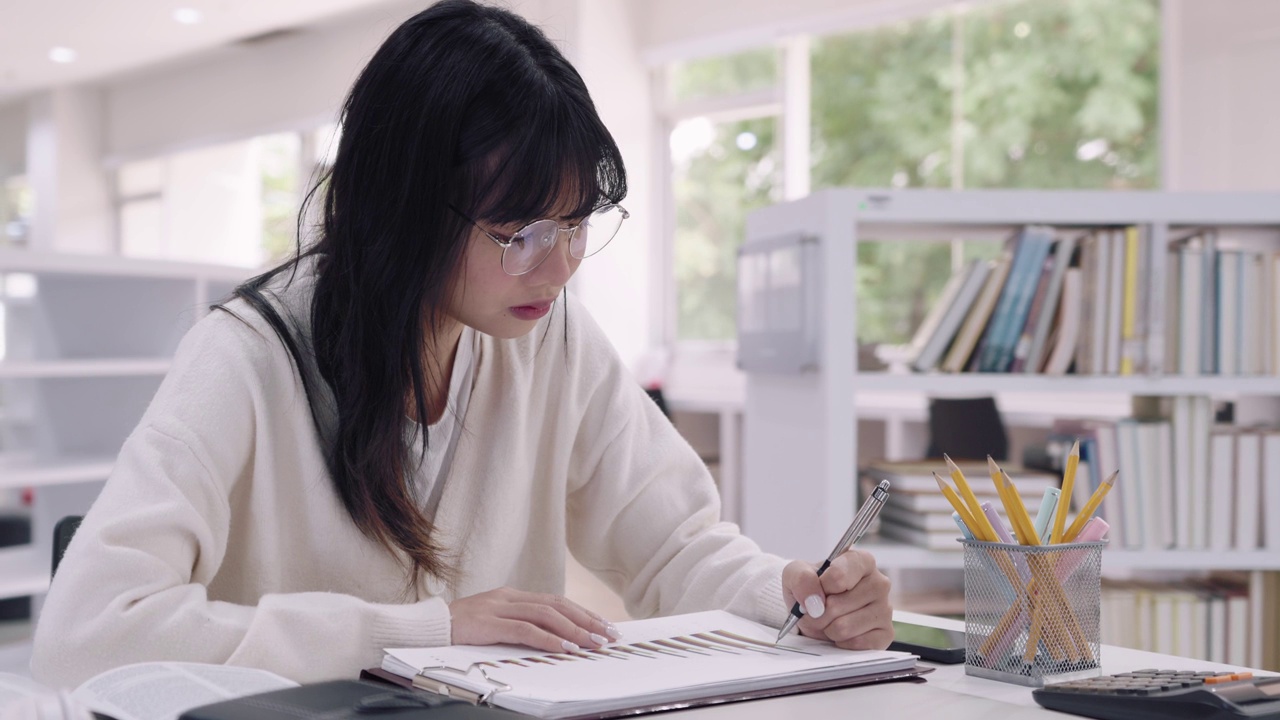 亚洲女大学生正在大学图书馆认真学习和理解课程，准备作业或考试。抓住焦点。视频素材