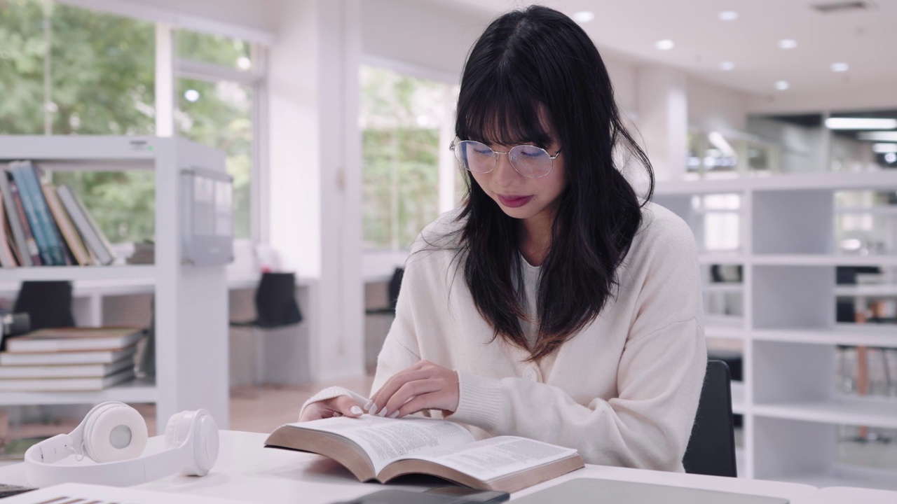 年轻的亚洲女大学生沉浸在学习中，阅读书籍研究和探索额外的课程，在大学图书馆准备考试。他们专注于学术探究和考试准备视频素材