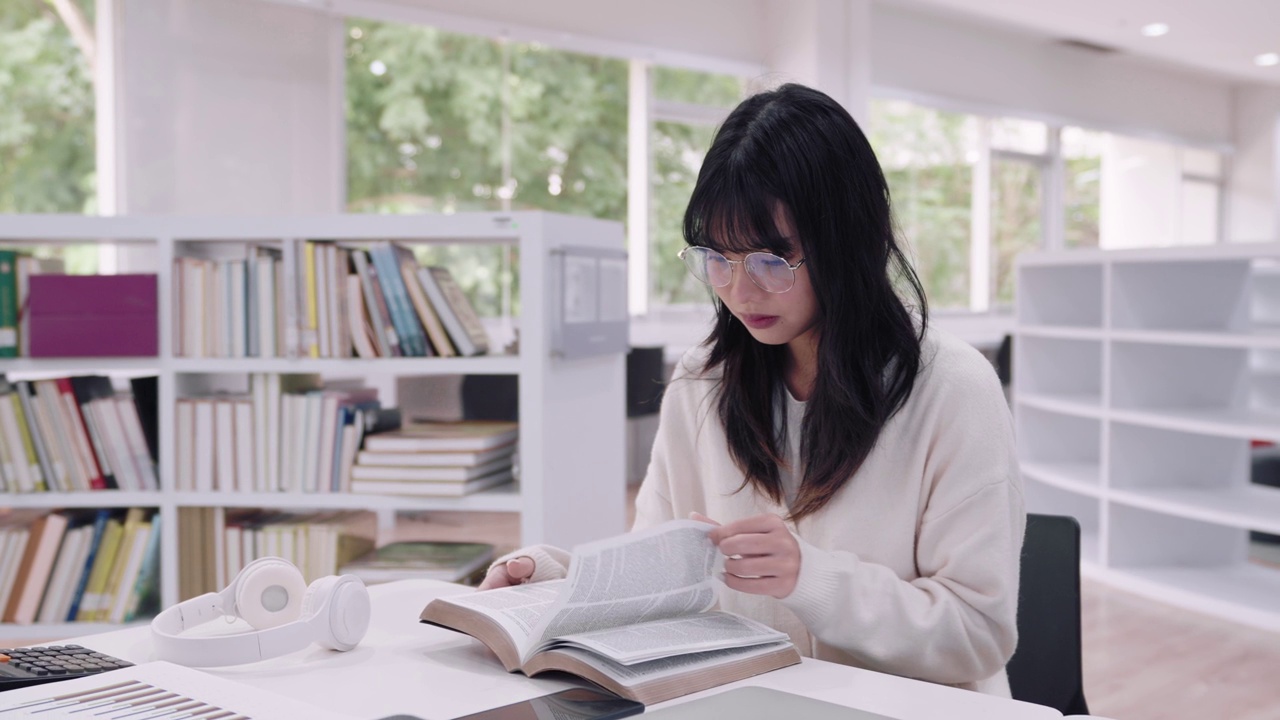 年轻的亚洲女大学生沉浸在学习中，阅读书籍研究和探索额外的课程，在大学图书馆准备考试。他们专注于学术探究和考试准备视频素材