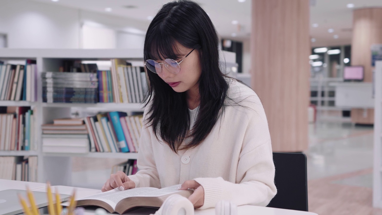 年轻的亚洲女大学生沉浸在学习中，阅读书籍研究和探索额外的课程，在大学图书馆准备考试。他们专注于学术探究和考试准备视频素材