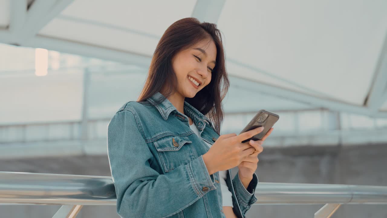 年轻的亚洲女子站在城市里，在街上使用手机视频素材