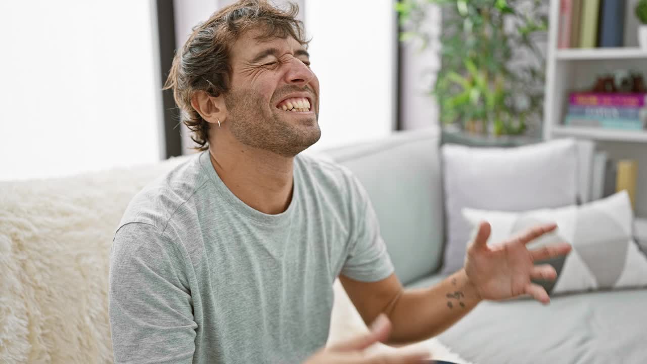 兴奋的年轻人在沙发上庆祝疯狂的成功!高举双臂，欢庆胜利，欣喜若狂。室内画像英俊的获胜者在家里。视频素材