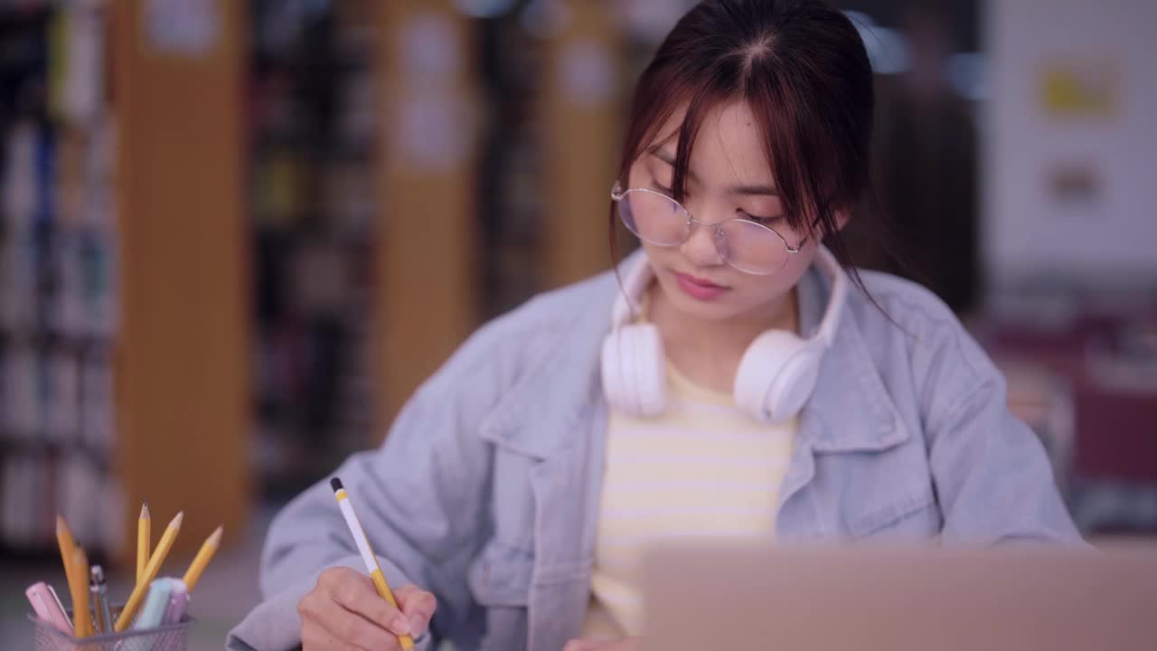 专注的亚洲女学生进行研究，收集信息，并在大学图书馆的笔记本上记录调查结果。在学术环境中孜孜不倦地追求知识和学术卓越视频素材