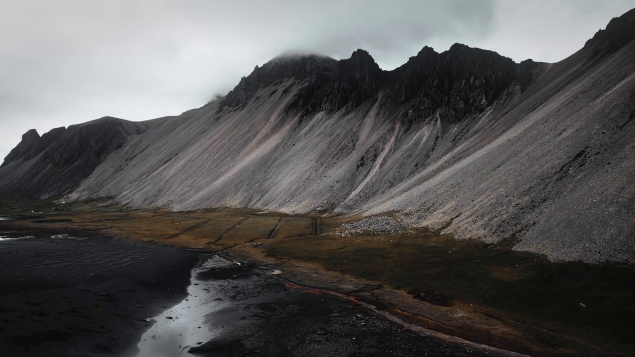 空中黑色的沙滩沙滩，黑色的火山山脉，绿色的橙草，黑暗忧郁多云的景色，冰岛视频素材