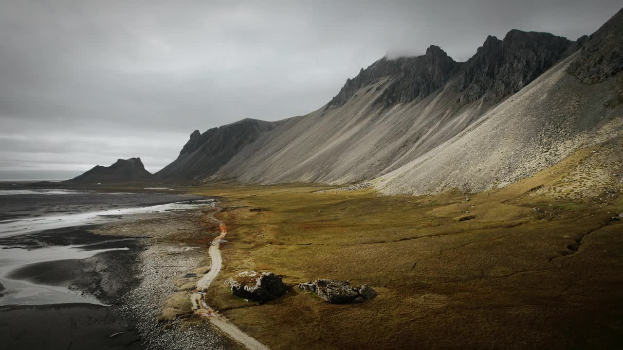 空中黑色的沙滩上有白鹤，黑色的火山山脉上有绿油油的橙草，黑暗阴沉的冰岛多云的景色视频素材