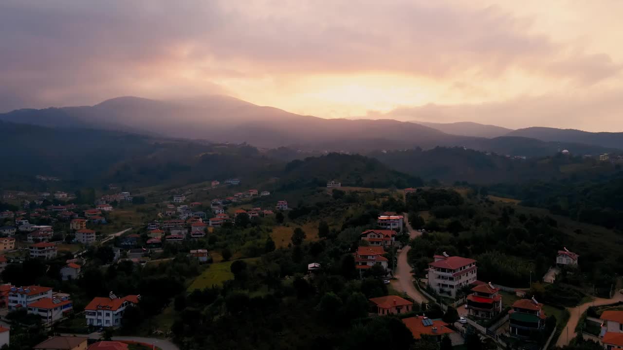 无人机拍摄的山腰村庄，背景是多云的黄昏天空下的山脉视频素材