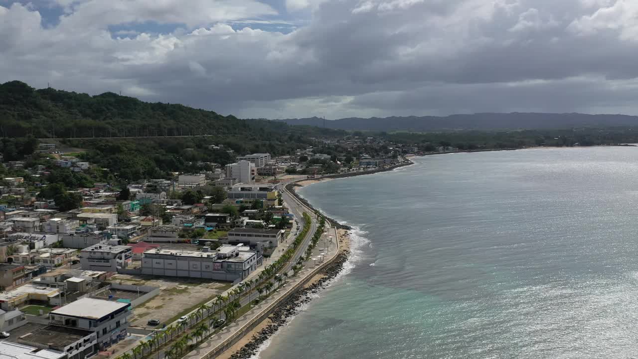 无人机拍摄的汽车行驶在波多黎各阿瓜迪拉沿海道路和海滨建筑上的画面视频素材