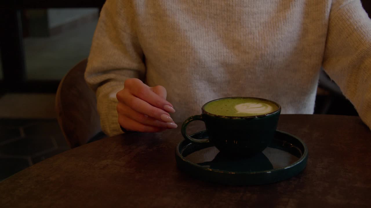 年轻女子坐在咖啡馆里准备喝抹茶拿铁和泡沫艺术。视频素材