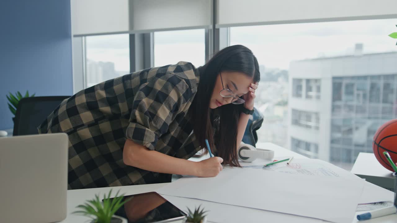 眼镜建筑师在窗户的工作场所绘制蓝图。女性写作计划视频素材