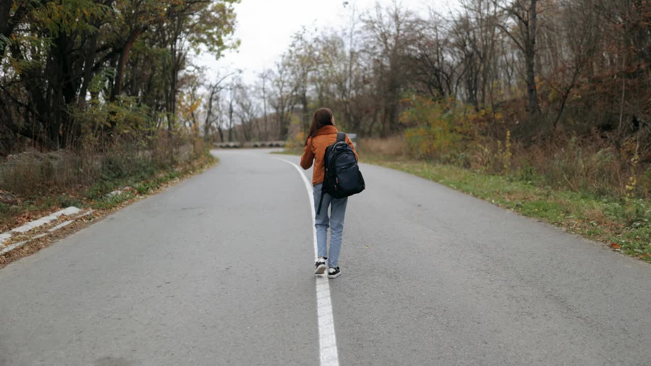 年轻的女性旅行者带着相机，拍摄鸟类，动物，风景。秋天，一名女游客背着背包独自在路上旅行，用相机拍照视频素材