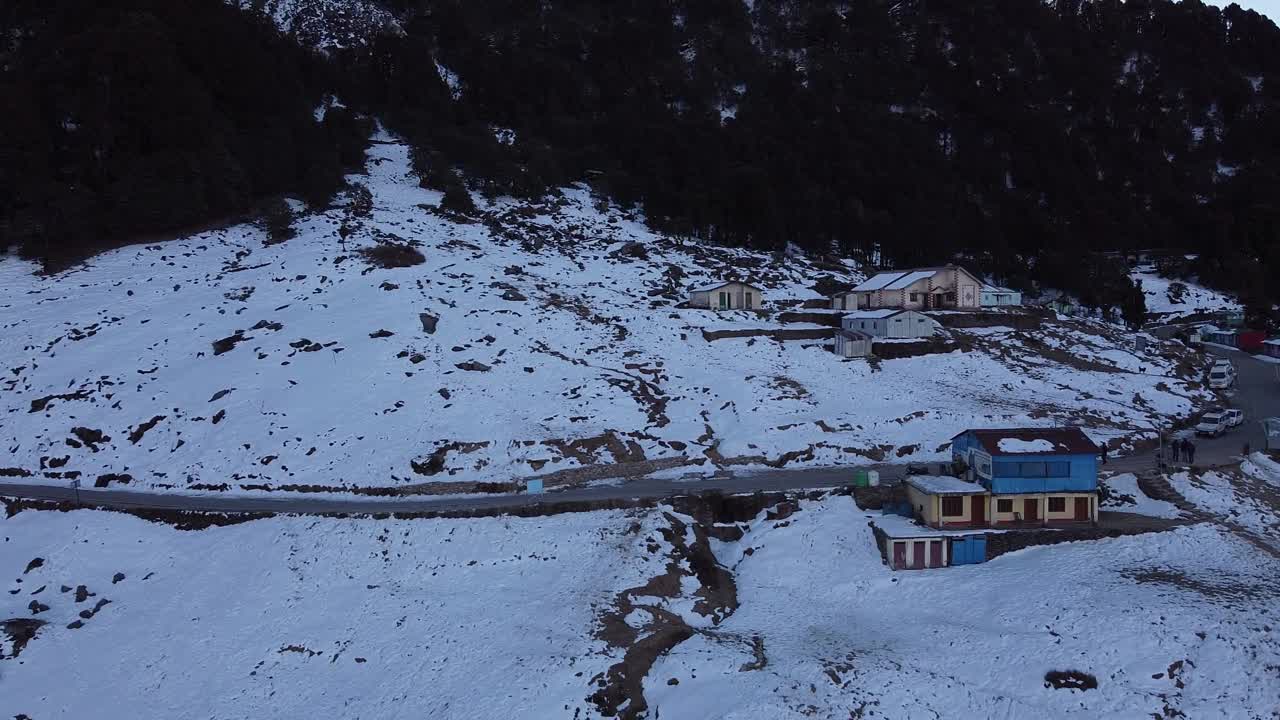 无人机拍摄的一条狭窄的柏油路穿过被雪覆盖的山腰村庄视频素材