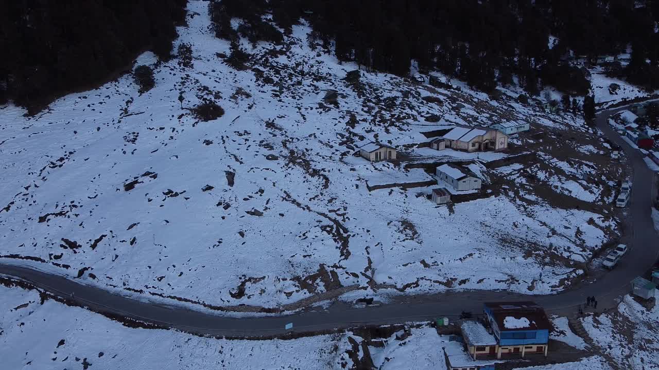 无人机拍摄的一条狭窄的柏油路穿过被雪覆盖的山腰村庄视频素材