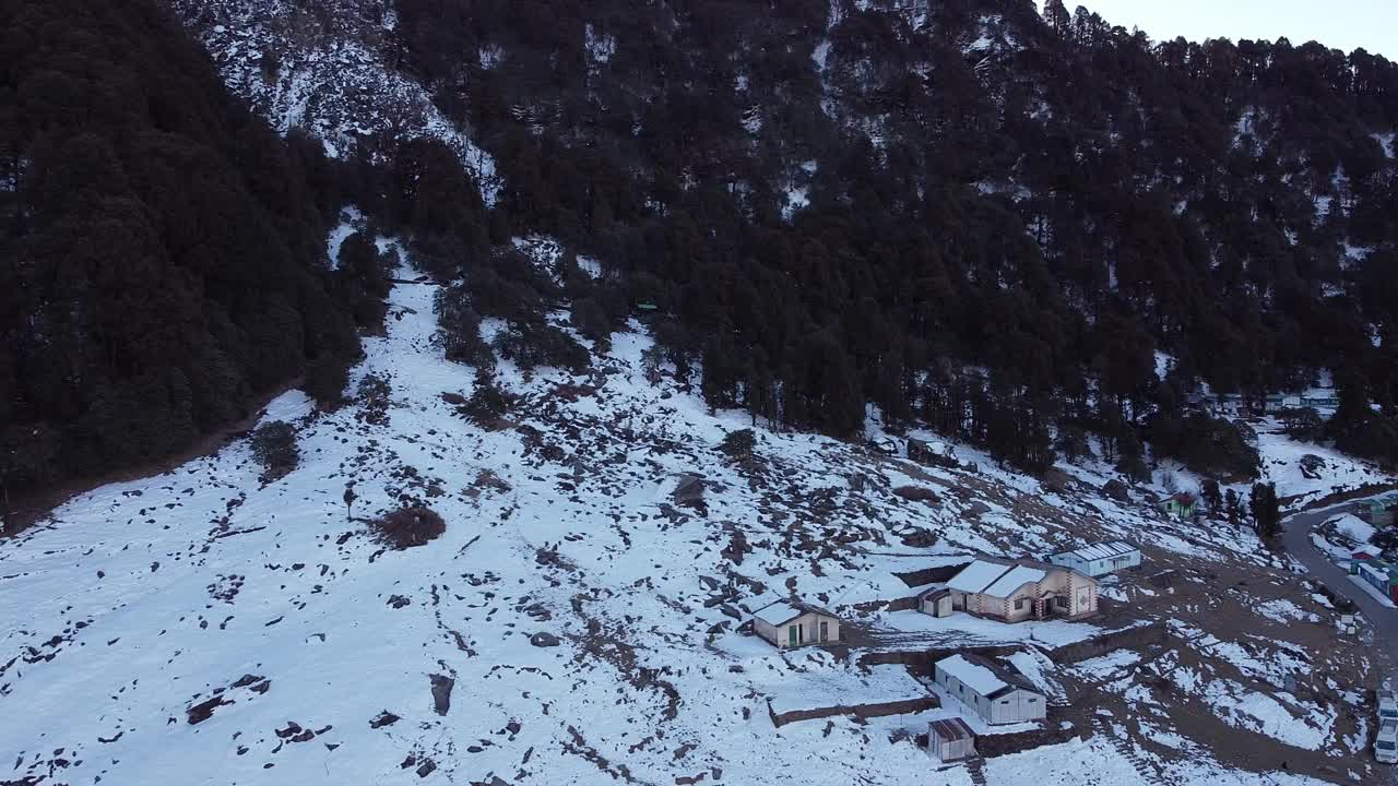 无人机拍摄的山腰村庄的房屋被雪覆盖，背景是森林视频素材