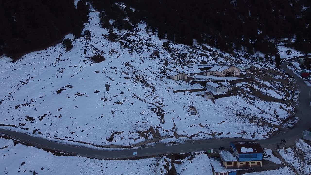 无人机拍摄的一条狭窄的柏油路穿过被雪覆盖的山腰村庄视频素材