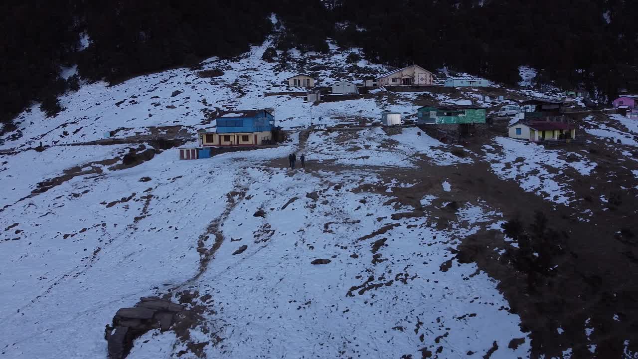 无人机拍摄的四个人走在被雪覆盖的山腰村庄的小路上视频素材