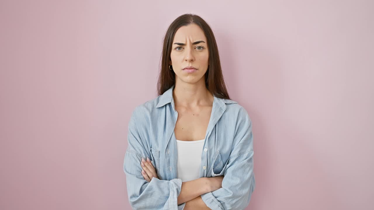 令人难以置信的是，一位年轻美丽的西班牙女子的肖像，双臂交叉，在粉红色的背景下穿着运动服。紧张、消极的气氛笼罩着她怀疑、不赞成的表情。视频素材