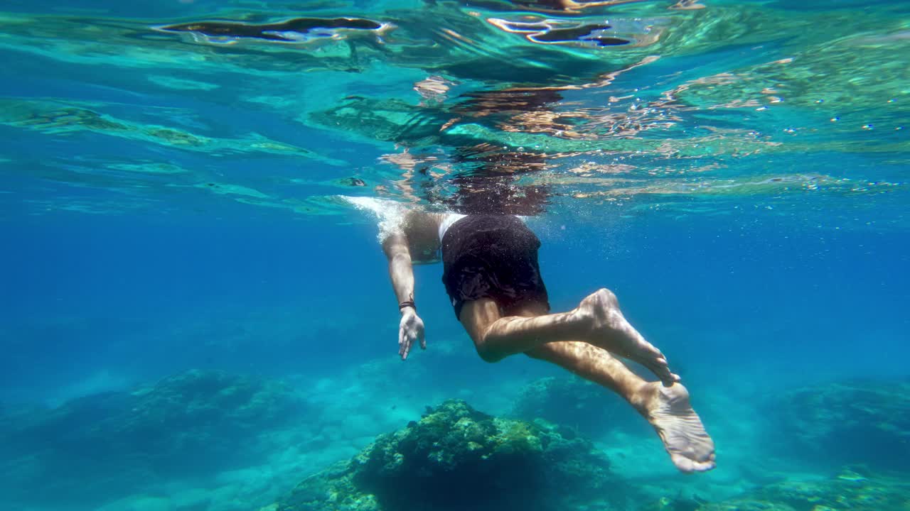 男子在蓝色的海底浮潜游泳。和一个人在海水里自由潜水。在深海中浮潜和潜水。浅水中的海洋生物。在珊瑚礁附近游泳的人慢动作4k视频素材