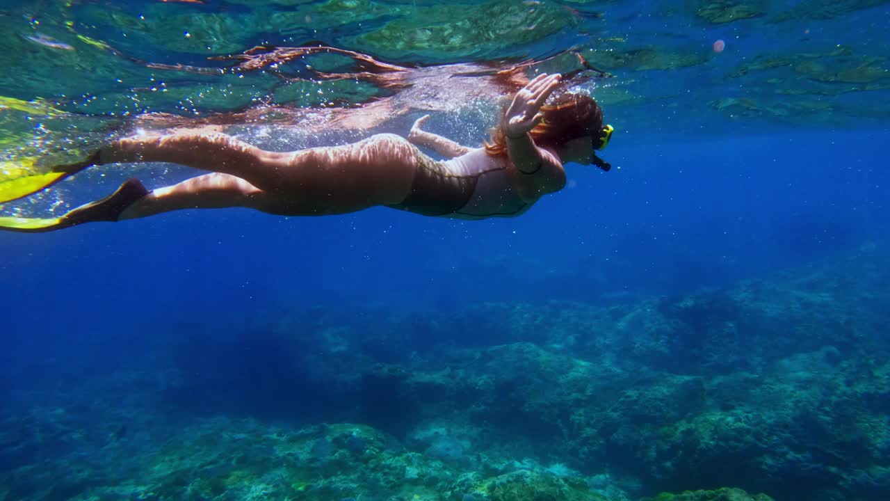 女子在蓝色的海水下浮潜游泳。和女孩一起在海水里自由潜水。在深海中浮潜和潜水。浅水中的海洋生物。在珊瑚礁附近游泳的人慢动作4k视频素材