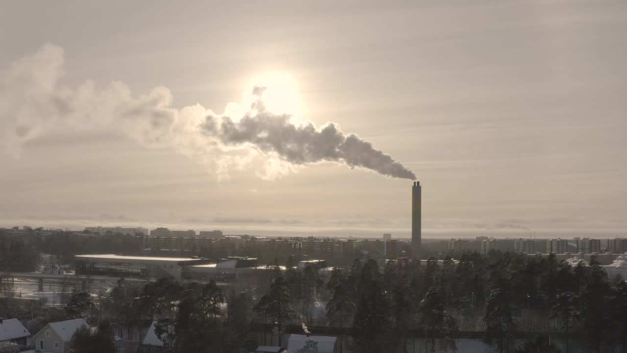 在一个多雪的城市冬季景观中，阳光照射下的烟雾从烟囱中冒出。视频下载